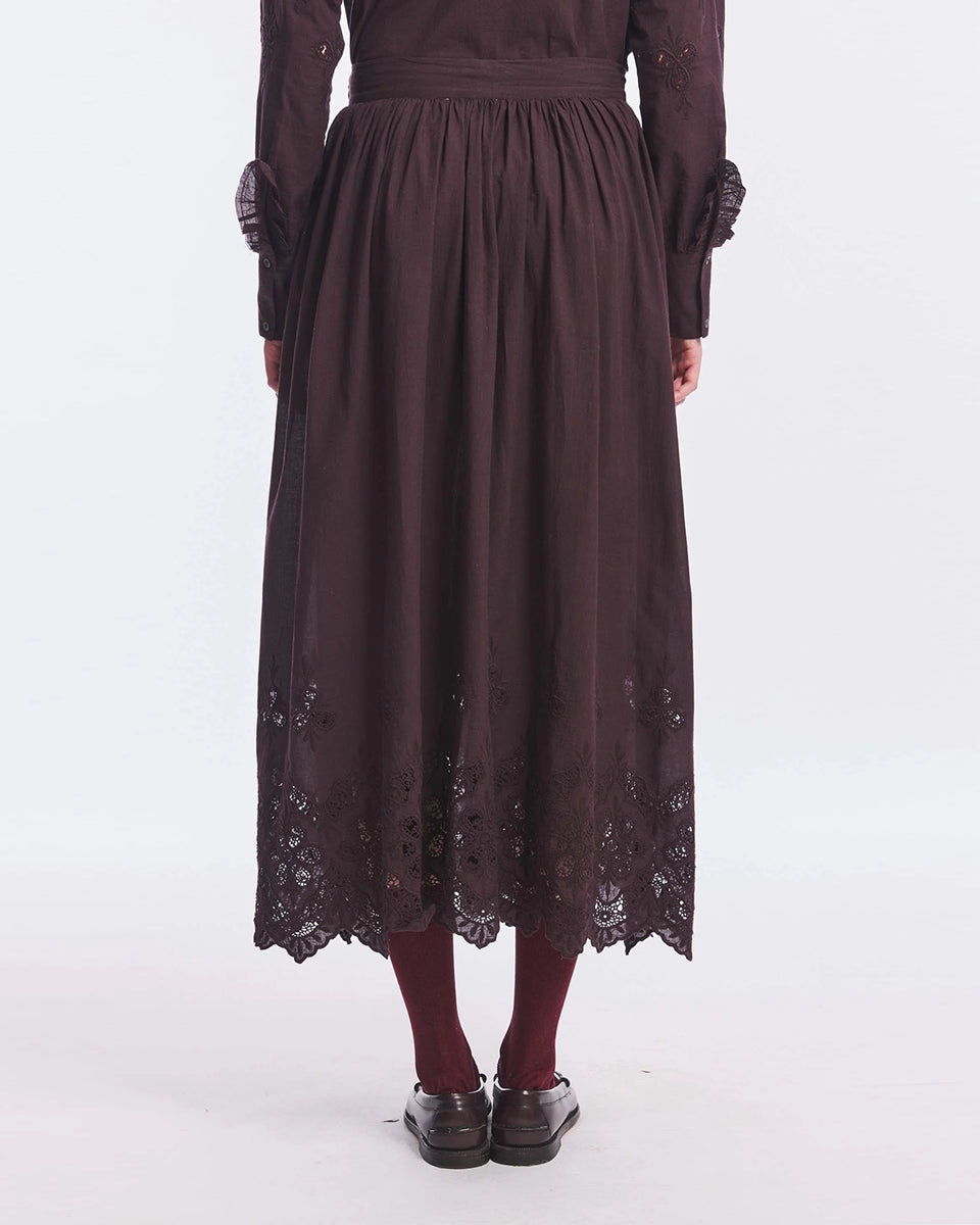 Długa, podszyta, bawełniana spódnica Albertine Antik Batik Plum z ażurowym haftem na dole. Posiada kieszenie boczne oraz zapięcie na suwak i haftkę. Ma wszytą halkę. Objętość modelu podkreślają delikatne marszczenia w talii, nadające całości lekkości i zwiewności. Ma długość do polowy łydki.