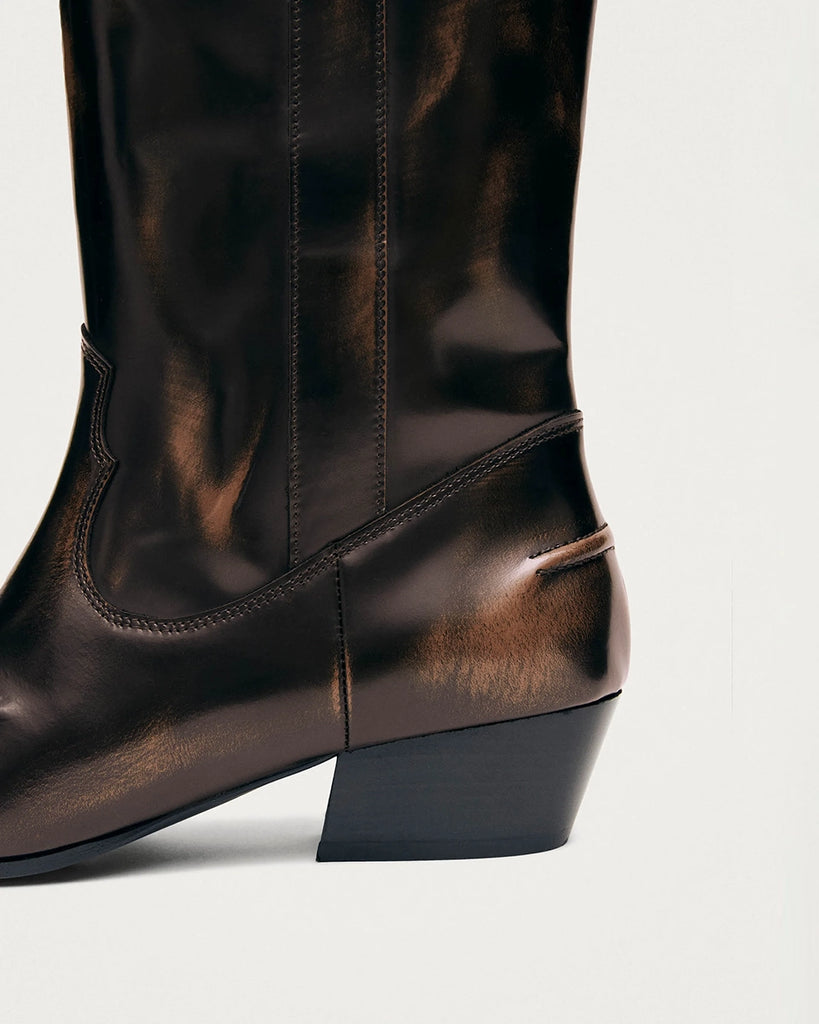 Bordowe, skórzane kowbojki ALOHAS Chase Brushed Burgundy o szczotkowym wykończeniu, z subtelnym połyskiem. Charakteryzują się wydłużonym, kwadratowym noskiem i przeszyciem wzdłuż górnej krawędzi. Sięgają do łydki. Po bokach posiadają uchwyty z logo marki, które ułatwiają zakładanie.