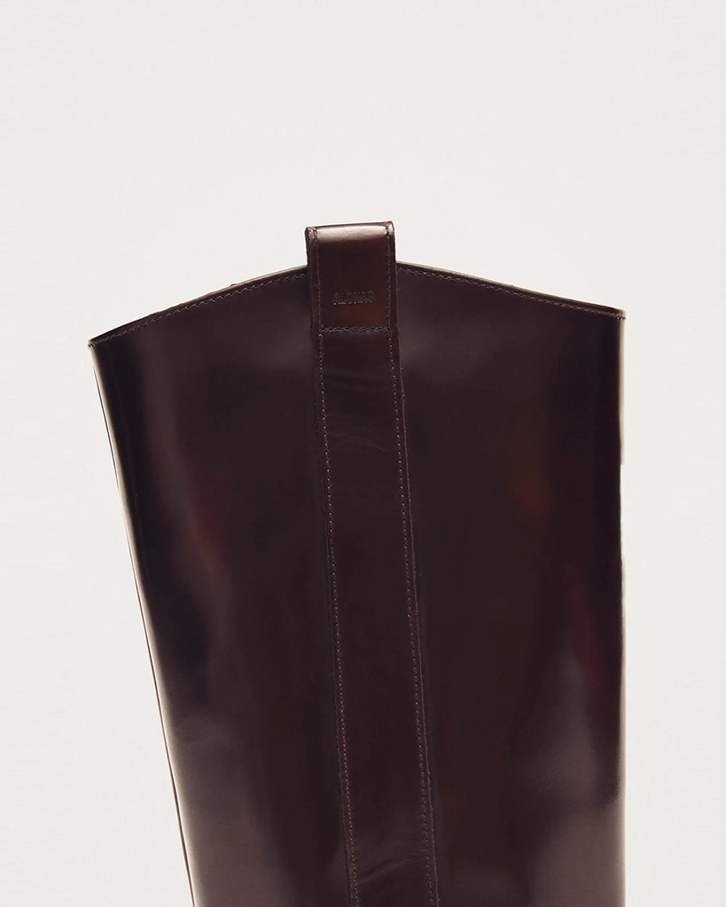 Bordowe, skórzane kowbojki ALOHAS Chase Brushed Burgundy o szczotkowym wykończeniu, z subtelnym połyskiem. Charakteryzują się wydłużonym, kwadratowym noskiem i przeszyciem wzdłuż górnej krawędzi. Sięgają do łydki. Po bokach posiadają uchwyty z logo marki, które ułatwiają zakładanie.