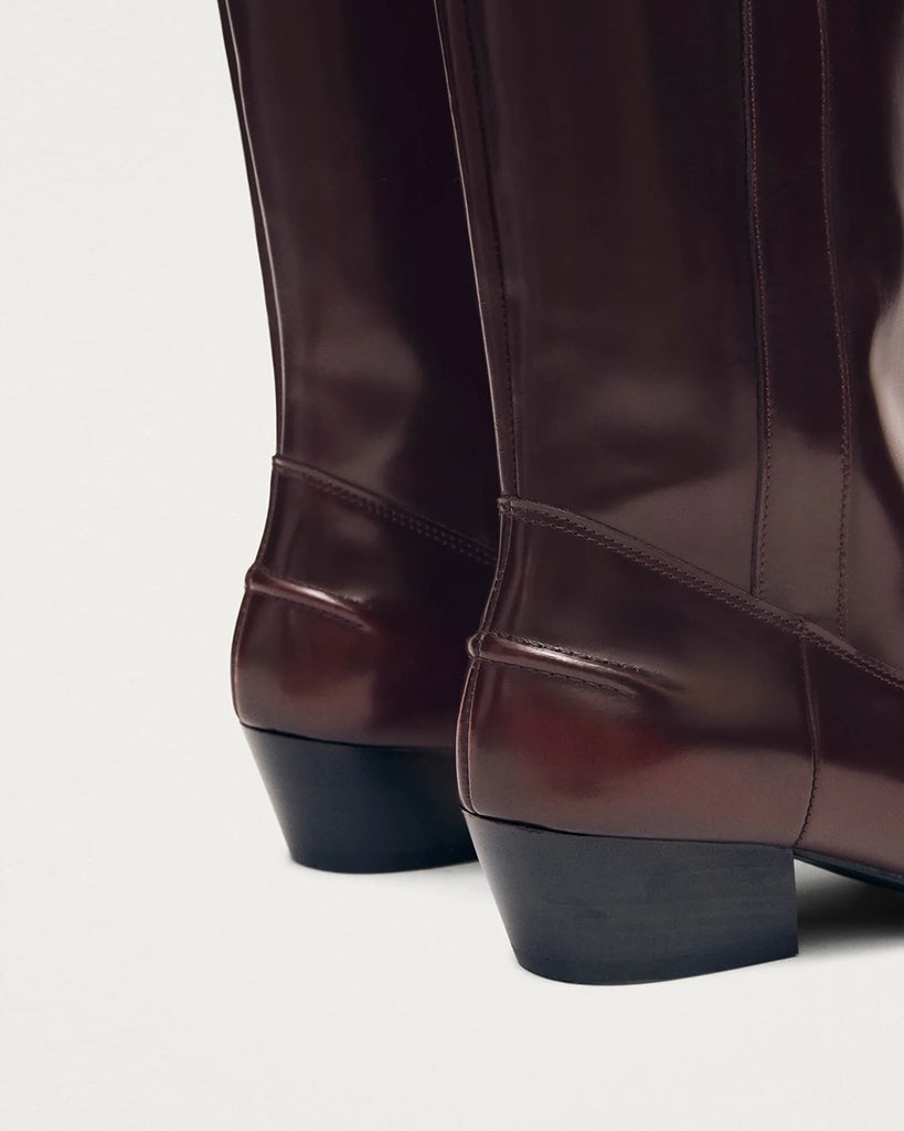 Bordowe, skórzane kowbojki ALOHAS Chase Brushed Burgundy o szczotkowym wykończeniu, z subtelnym połyskiem. Charakteryzują się wydłużonym, kwadratowym noskiem i przeszyciem wzdłuż górnej krawędzi. Sięgają do łydki. Po bokach posiadają uchwyty z logo marki, które ułatwiają zakładanie.