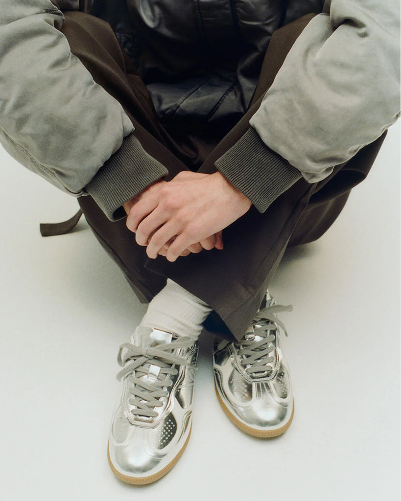 Srebrne, skórzane trampki ALOHAS TB.490 Silver Cream z kontrastowymi detalami, na płaskiej gumowej podeszwie. Posiadają okrągłe noski. Wykonane ze srebrnej skóry z połyskiem. Wiązane na sznurówki.
