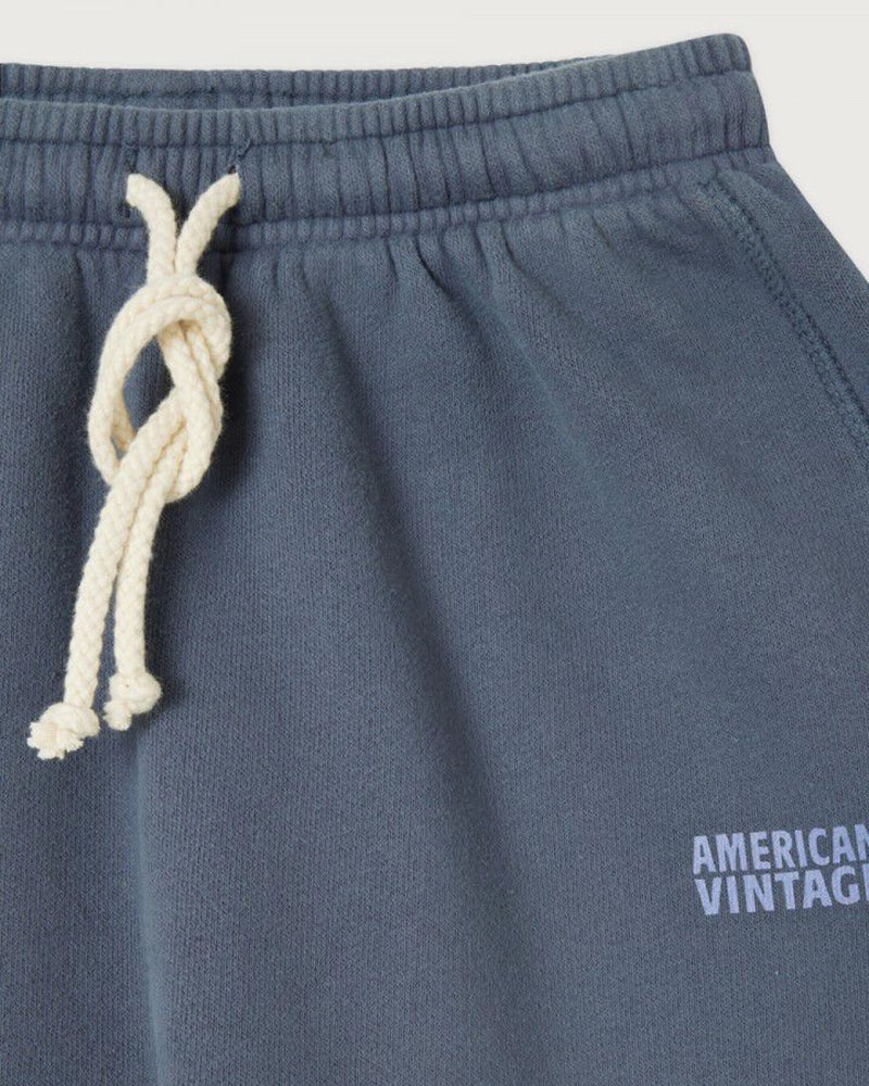 Luźne, bawełniane spodnie dresowe IZUBIRD American Vintage z wysokim stanem i szeroką, lekko skróconą nogawką. Wiązane i elastyczne w talii. Na lewej nogawce spodnie mają niewielkie logo marki.