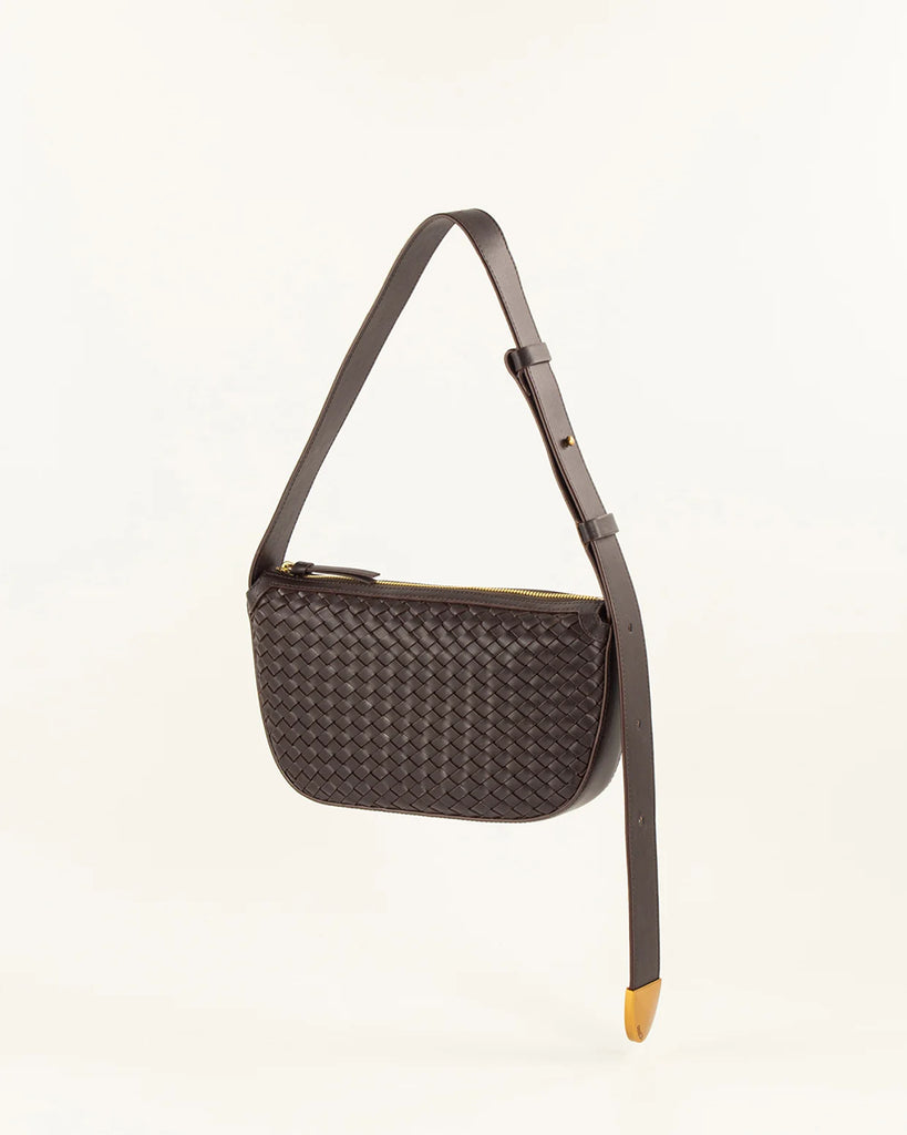 Brązowa skórzana torebka Amo Deep Coffee typu baguette marki Sessun z ręcznie plecionym panelem z przodu. Posiada kieszeń centralną z dodatkową kieszenią naszytą i regulowany pasek na ramię, z zapięciem na ćwieki oraz metalowym, złotym zakończeniem z logo marki.