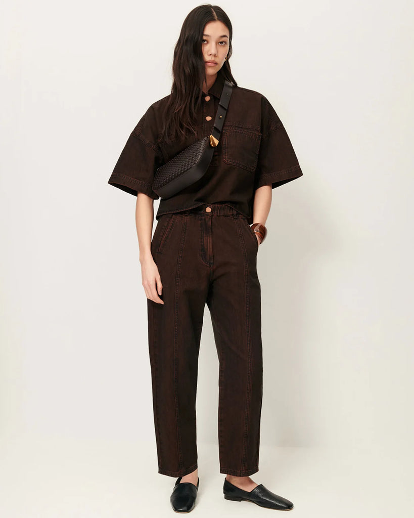 Brązowa skórzana torebka Amo Deep Coffee typu baguette marki Sessun z ręcznie plecionym panelem z przodu. Posiada kieszeń centralną z dodatkową kieszenią naszytą i regulowany pasek na ramię, z zapięciem na ćwieki oraz metalowym, złotym zakończeniem z logo marki.