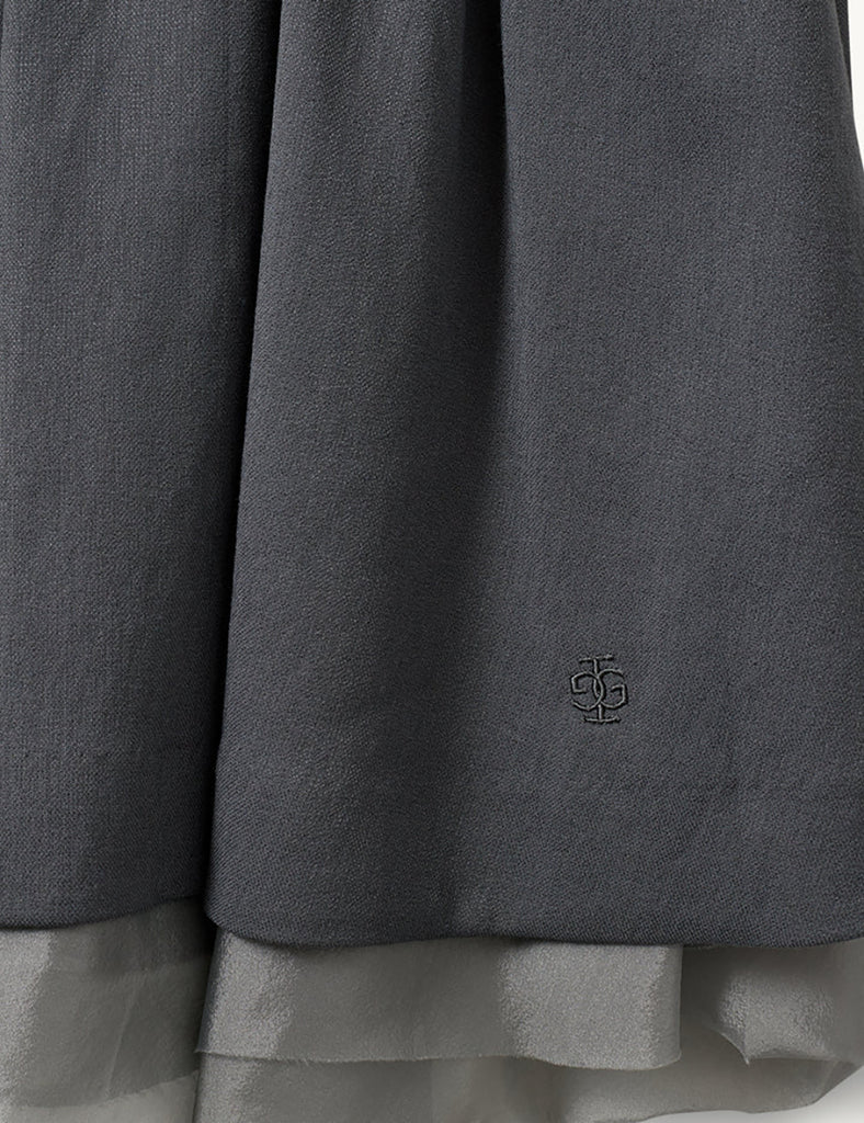 Szara, rozkloszowana spódnica Andrea Midi Charcoal o delikatnej fakturze, sięgająca do kolan. Pod spodem widoczna jest warstwa cienkiej siateczki, co dodaje dziewczęcego charakteru. Talia spódnicy jest lekko podkreślona. Po lewej stronie u dołu znajduje się mały haft z logo marki. Całość wygląda bardzo lekko i romantycznie.