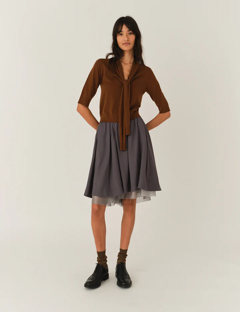 Szara, rozkloszowana spódnica Andrea Midi Charcoal o delikatnej fakturze, sięgająca do kolan. Pod spodem widoczna jest warstwa cienkiej siateczki, co dodaje dziewczęcego charakteru. Talia spódnicy jest lekko podkreślona. Po lewej stronie u dołu znajduje się mały haft z logo marki. Całość wygląda bardzo lekko i romantycznie.