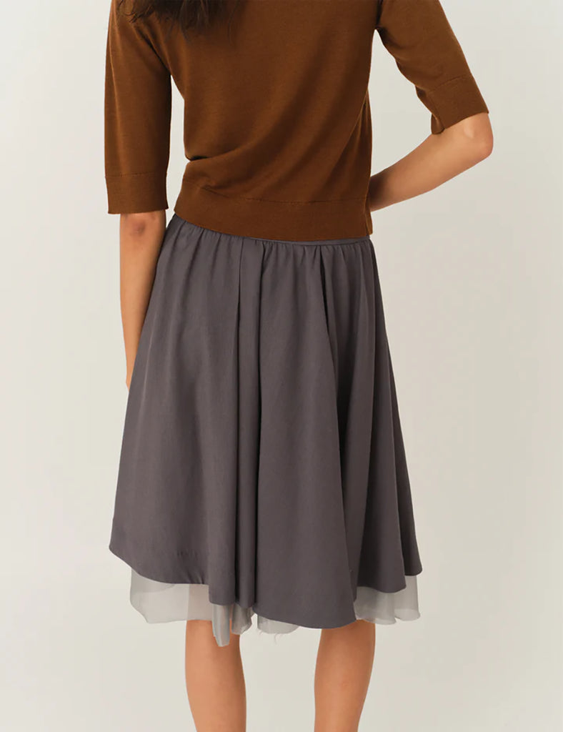 Szara, rozkloszowana spódnica Andrea Midi Charcoal o delikatnej fakturze, sięgająca do kolan. Pod spodem widoczna jest warstwa cienkiej siateczki, co dodaje dziewczęcego charakteru. Talia spódnicy jest lekko podkreślona. Po lewej stronie u dołu znajduje się mały haft z logo marki. Całość wygląda bardzo lekko i romantycznie.