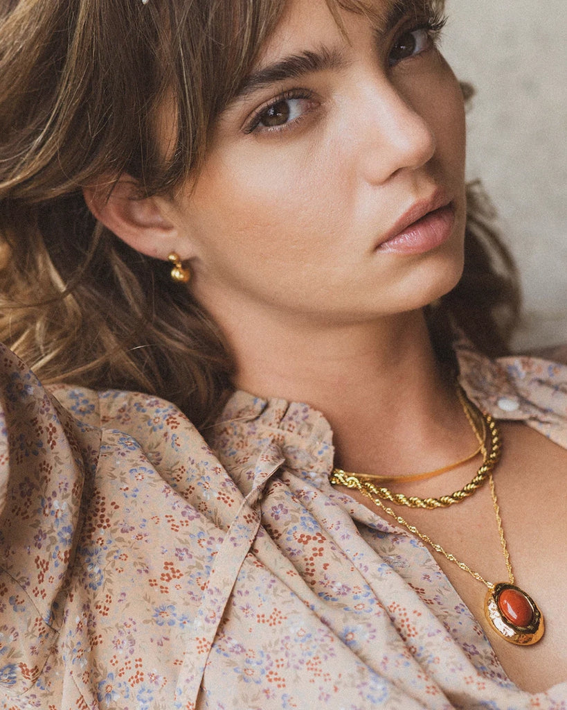 Elegancki, pozłacany naszyjnik Cherry On Top Anni Lu na długim, skręconym łańcuszku z efektowną zawieszką z dużym owalnym jaspisem. Wykończony niewielką, naturalną perłą słodkowodną.