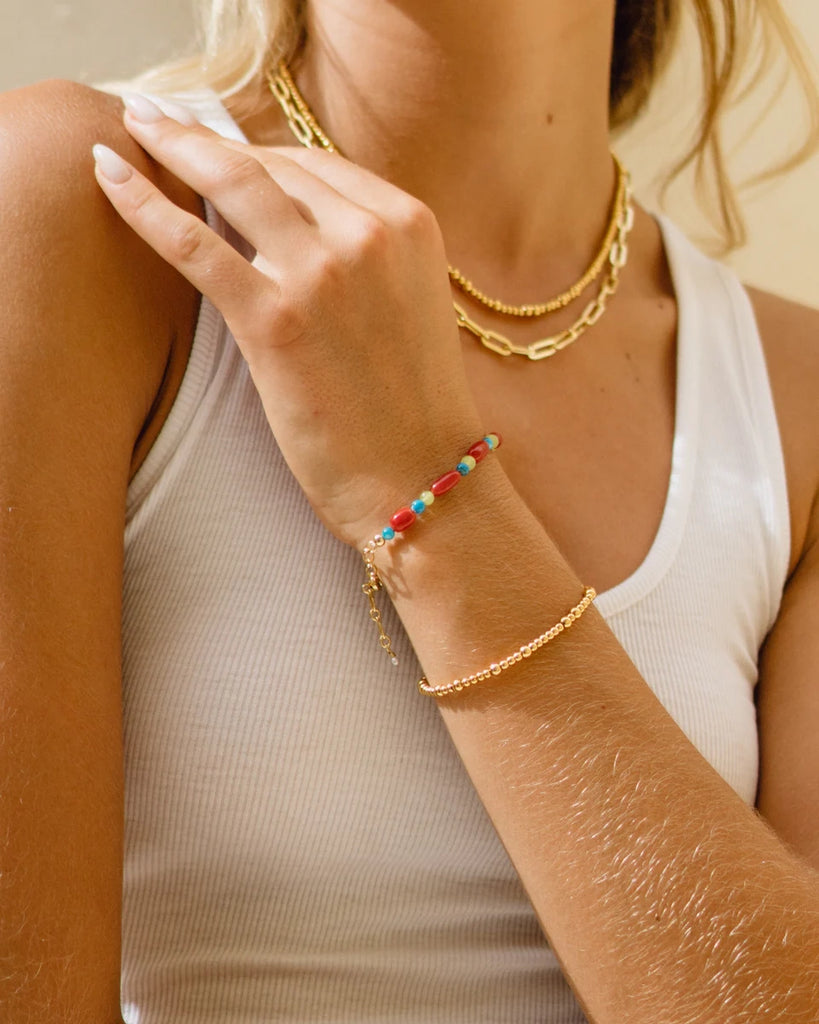 Kolorowa bransoletka Red Crush ANNI LU z dużymi kamieniami półszlachetnymi o nieregularnych kształtach i koralikami z barwionej masy perłowej. Wykończona pozłacanym łańcuszkiem o regulowanej długości zakończonym małą perłą naturalną.