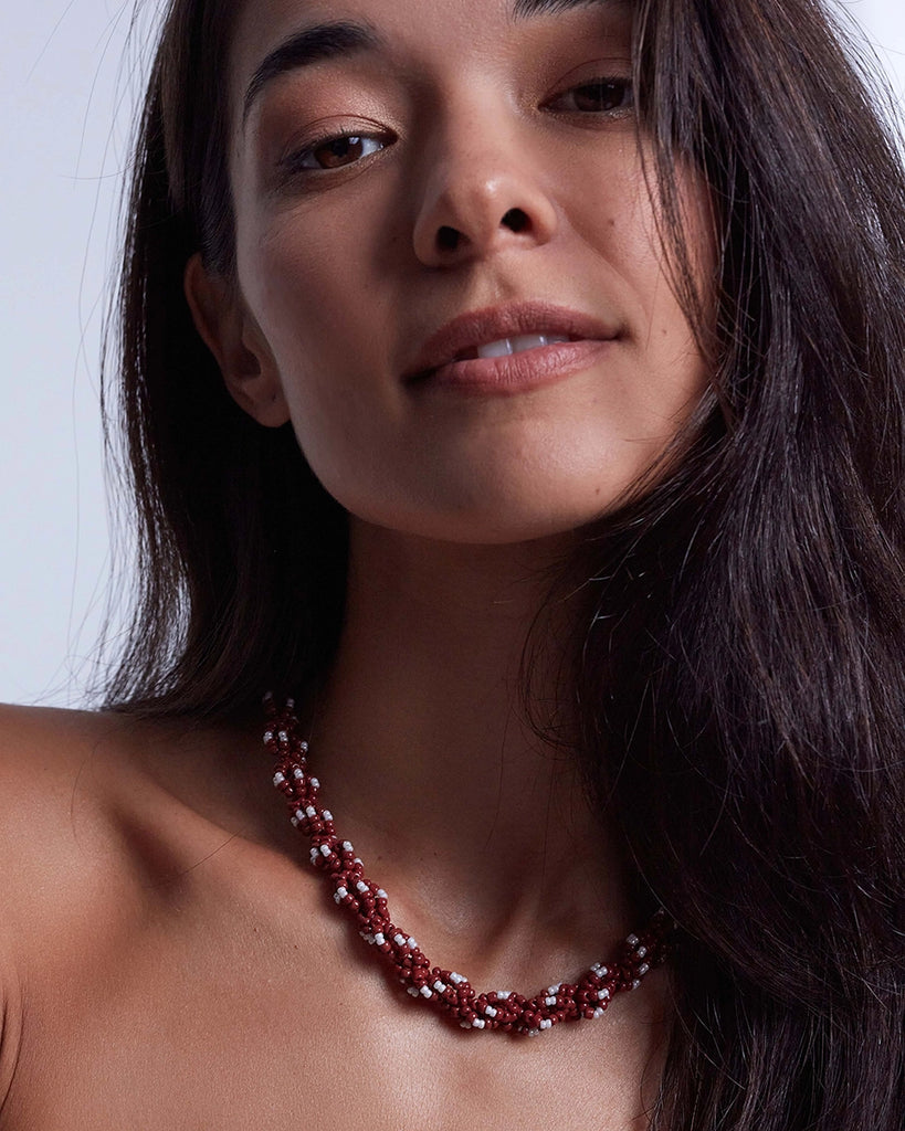 Gruby, efektowny naszyjnik o skręconym splocie Rodeo Anni Lu wykonany drobnych koralików w pięknym, burgundowym kolorze. Wykończony pozłacanym łańcuszkiem o regulowanej długości z niewielką, naturalną perłą na jego końcu.