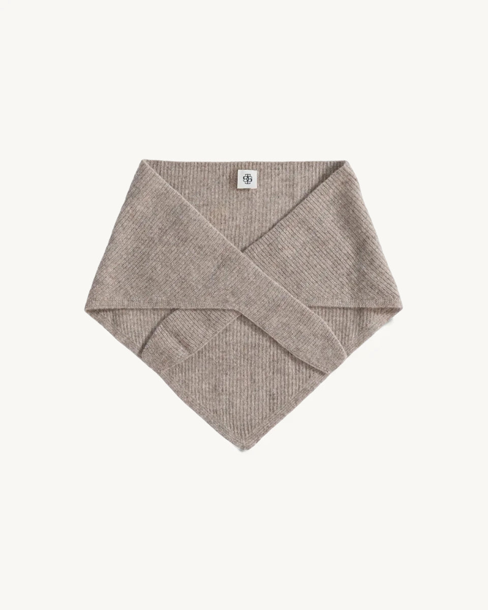 Dzianinowy, beżowy szalik Como Bandana Scarf w kształcie bandany, który charakteryzuje się gładką strukturą. Składa się z trójkątnej części głównej z dłuższymi troczkami zaprojektowanymi do owinięcia pod szyją, co pozwala na naturalne i schludne układanie się materiału. Wykonany z 95% wełny oraz 5% kaszmiru, co zapewnia mu miękkość i ciepło.&nbsp;