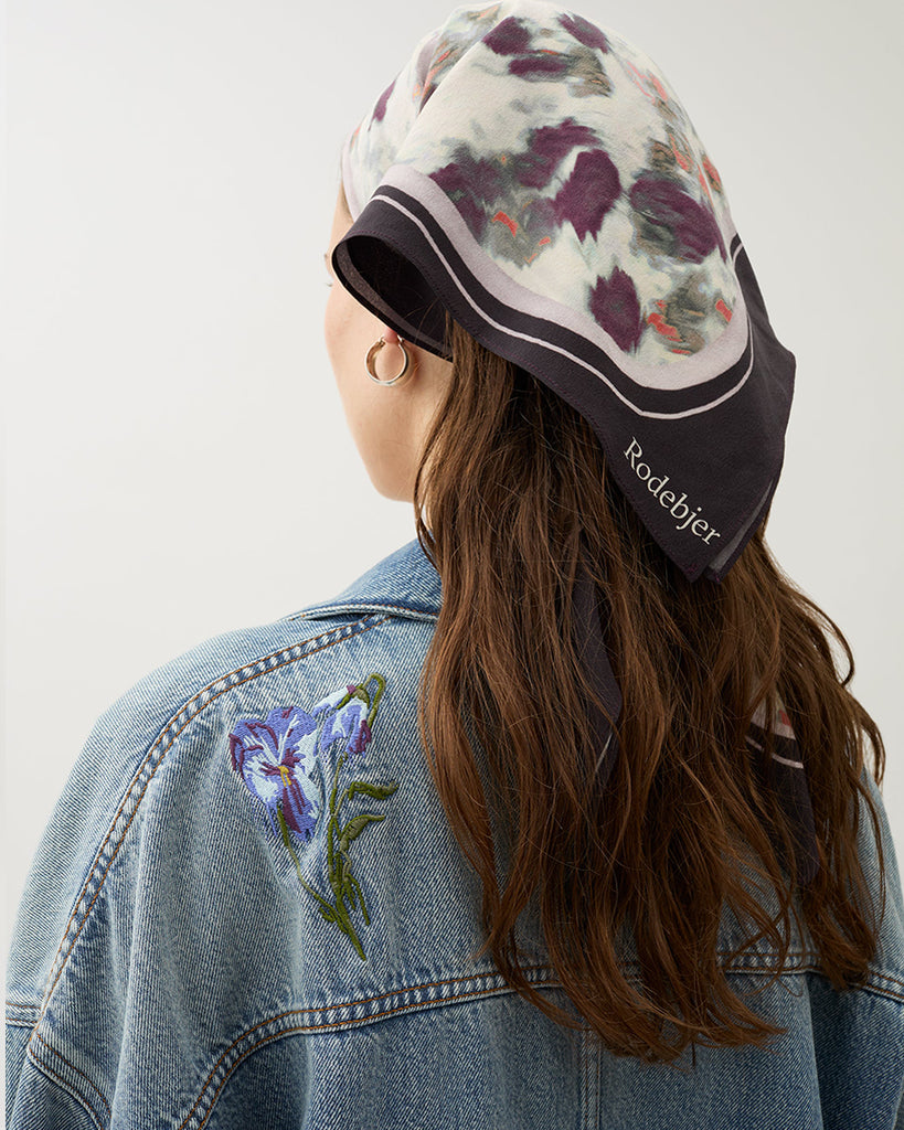 Oversizowa, jeansowa kurtka Bat Indigo w klasycznym, niebieskim odcieniu denimu z kwiatowymi haftami. Posiada lekko rozjaśnione partie na przodzie i rękawach, co tworzy wrażenie vintage. Ma obniżoną linię ramion i szerokie rękawy. Zapięcie na metalowe guziki typowe dla kurtki jeansowej oraz klasyczne kieszenie z patkami.&nbsp;