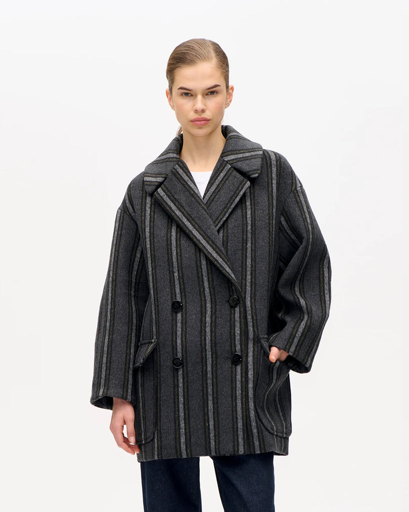 Luźny, prosty płaszcz Baticia Black Grey Stripe z klasycznym kołnierzem, dwurzędowym zapięciem na guziki i rozcięciem z tyłu, co nadaje mu ponadczasowy fason. Posiada dwie naszywane kieszenie z przodu. Długość midi. Wykonany z mieszanki wełny w paski.&nbsp;