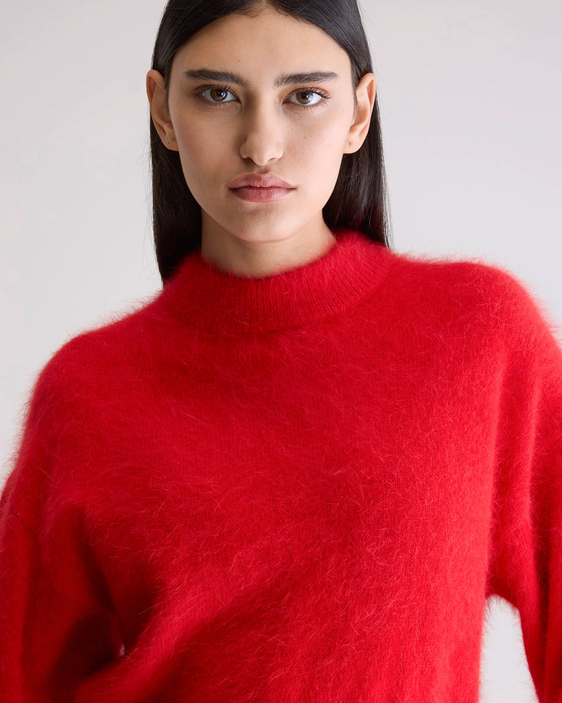 Prosty, krótki, czerwony sweter Dateka Bellerose z okrągłym dekoltem, opadającymi ramionami i szerokimi rękawami zakończonymi długimi, wąskimi ściągaczami. Sweter ma prosty krój i wykonany jest z bardzo miękkiej i puchatej dzianiny z angorą.