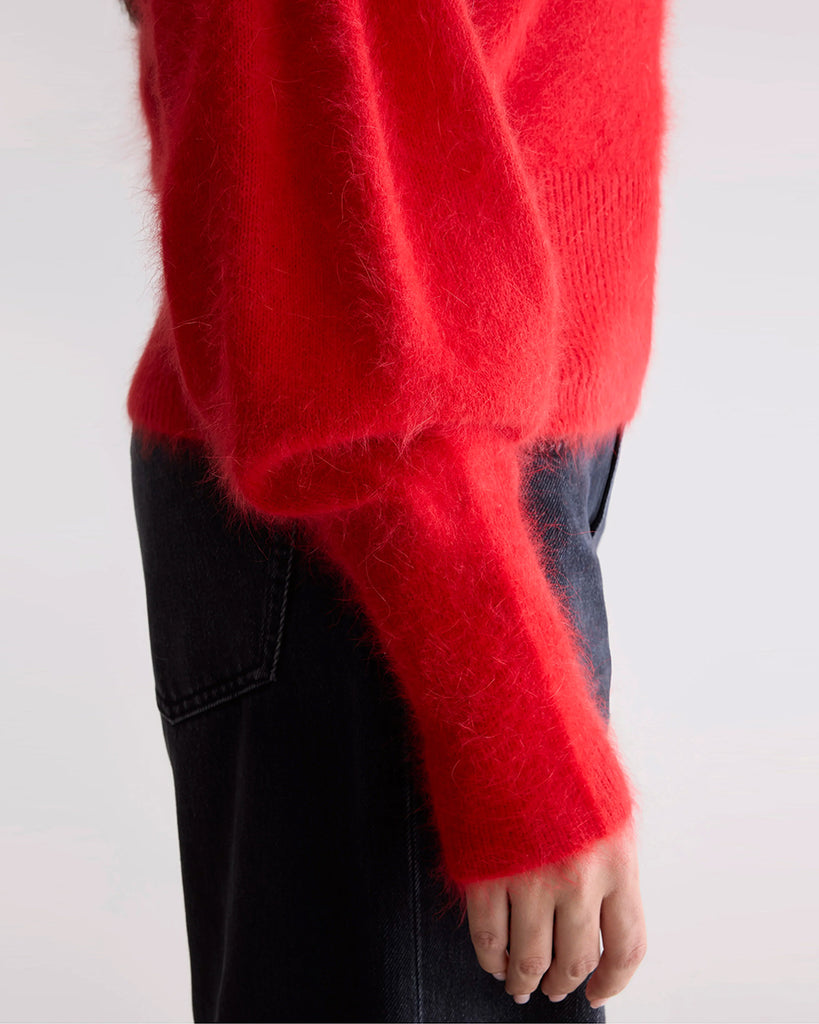 Prosty, krótki, czerwony sweter Dateka Bellerose z okrągłym dekoltem, opadającymi ramionami i szerokimi rękawami zakończonymi długimi, wąskimi ściągaczami. Sweter ma prosty krój i wykonany jest z bardzo miękkiej i puchatej dzianiny z angorą.