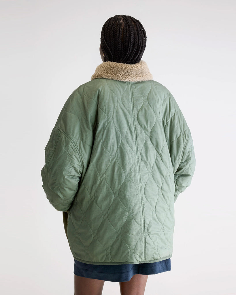 Oversizowa, dwustronna kurtka Hampton Bellerose w stylu worker. Posiada kołnierzyk i wywijane rękawy ze sztucznego kożucha. Z jednej strony wykonana ze śliskiej, pikowanej tkaniny w zielonym kolorze, z drugiej z patchworkowego materiału w różnych kolorach z elementami ze eko "misia"