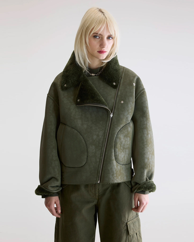Dwustronna, zielona kurtka z ekologicznego kożucha o kroju ramoneski Hedwee Bellerose z dużym kołnierzem, opadającymi ramionami i wywijanymi rękawami. Z przodu posiada dwie, duże kieszenie. Zapinany na idący na skos zamek błyskawiczny. Z jednej strony wykonany z imitacji skóry, z drugiej ze sztucznego, miłego w dotyku "misia".