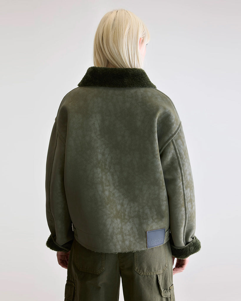 Dwustronna, zielona kurtka z ekologicznego kożucha o kroju ramoneski Hedwee Bellerose z dużym kołnierzem, opadającymi ramionami i wywijanymi rękawami. Z przodu posiada dwie, duże kieszenie. Zapinany na idący na skos zamek błyskawiczny. Z jednej strony wykonany z imitacji skóry, z drugiej ze sztucznego, miłego w dotyku "misia".