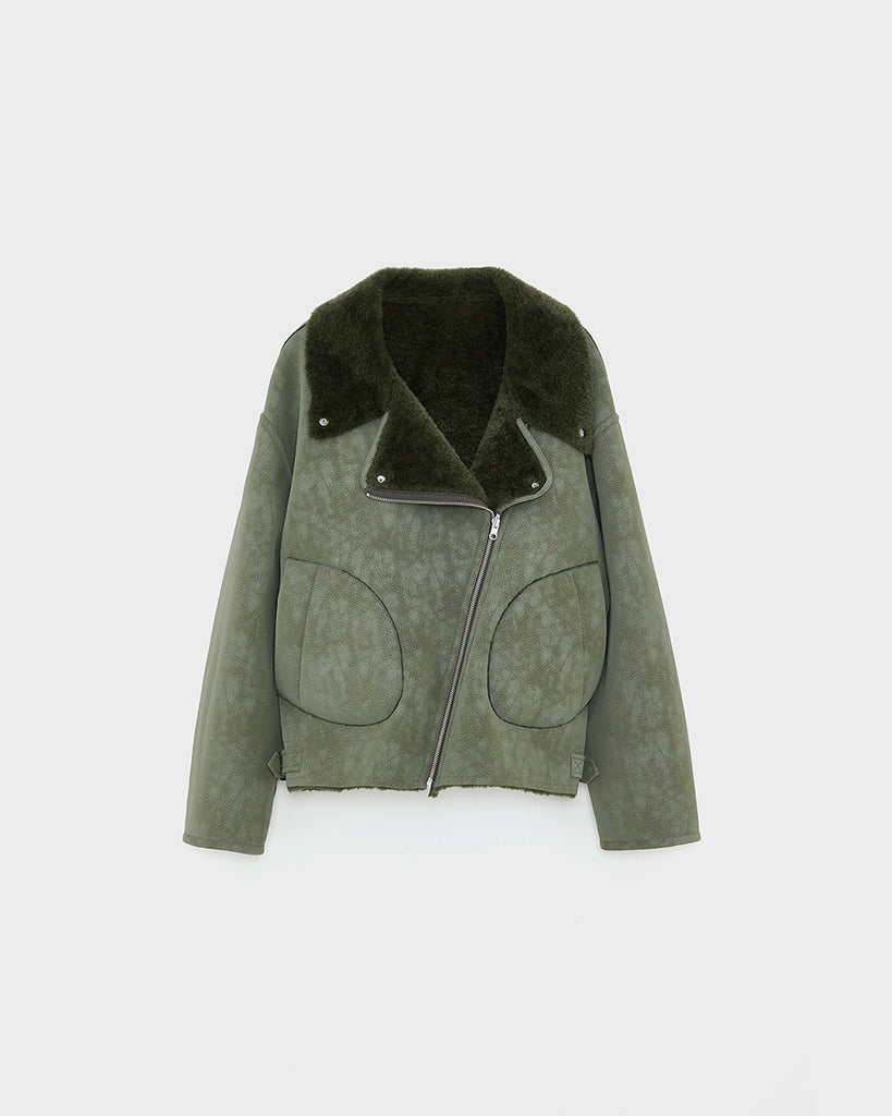 Dwustronna, zielona kurtka z ekologicznego kożucha o kroju ramoneski Hedwee Bellerose z dużym kołnierzem, opadającymi ramionami i wywijanymi rękawami. Z przodu posiada dwie, duże kieszenie. Zapinany na idący na skos zamek błyskawiczny. Z jednej strony wykonany z imitacji skóry, z drugiej ze sztucznego, miłego w dotyku "misia".