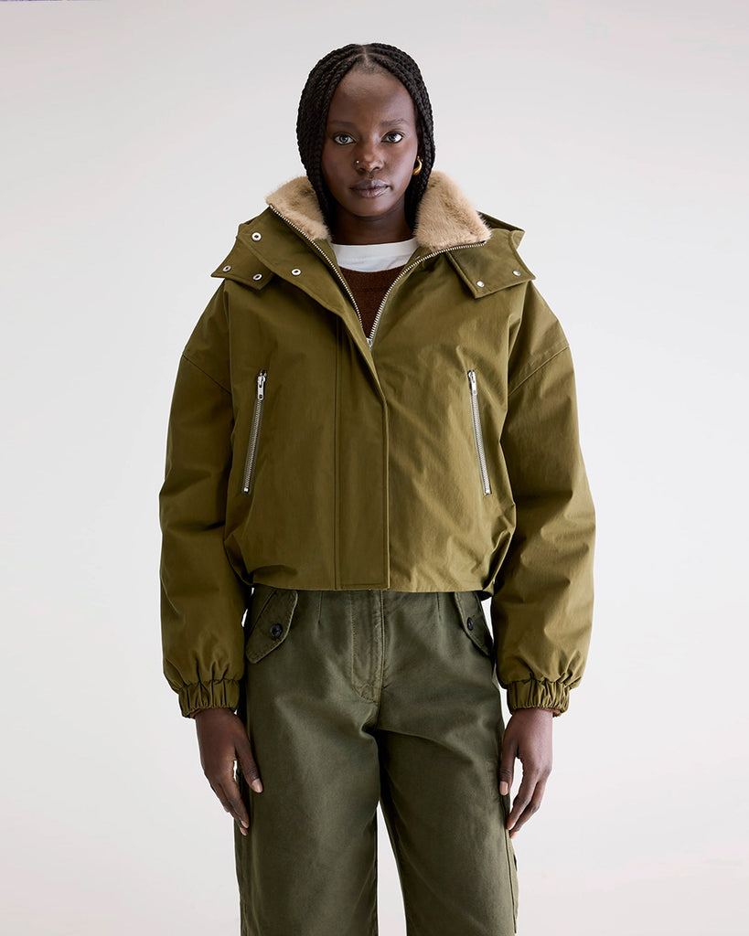 Krótka, ocieplana kurtka Herna Bellerose z kapturem i ciepłą podpinką ze sztucznego futra w kontrastowym kolorze. Kurtka ma opadające ramiona i szerokie rękawy zakończone elastycznym ściągaczem.