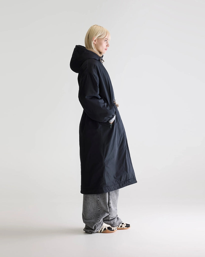 Długi, granatowy płaszcz Hosfo Bellerose z kapturem, wysokim kołnierzem podszyty sztucznym futrem w kontrastowym kolorze. Jednocześnie kobiecy i praktyczny. Zwężany i wiązany w talii. Wykonany z tkaniny z powłoką przeciwdeszczową. Płaszcz ma dwie, boczne kieszenie, rękawy wykończone ściągaczami i długość za kolana