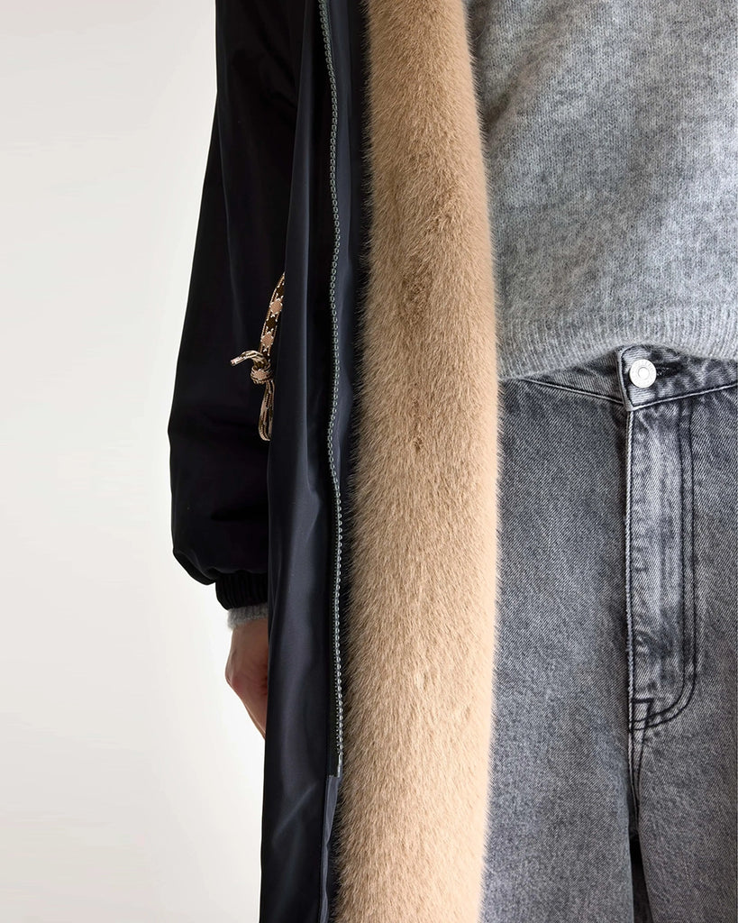 Długi, granatowy płaszcz Hosfo Bellerose z kapturem, wysokim kołnierzem podszyty sztucznym futrem w kontrastowym kolorze. Jednocześnie kobiecy i praktyczny. Zwężany i wiązany w talii. Wykonany z tkaniny z powłoką przeciwdeszczową. Płaszcz ma dwie, boczne kieszenie, rękawy wykończone ściągaczami i długość za kolana