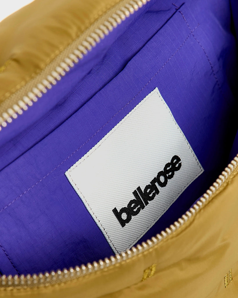 Pikowana, niewielka torebka-nerka Hosie Bellerose z miękkiej, "puchowej" tkaniny. Zapinana na zamek błyskawiczny. Wewnątrz obszyta kontrastową podszewką. Torebka ma szeroki, pleciony pasek o regulowanej długości do wygodnego przewieszenia przez ramię.