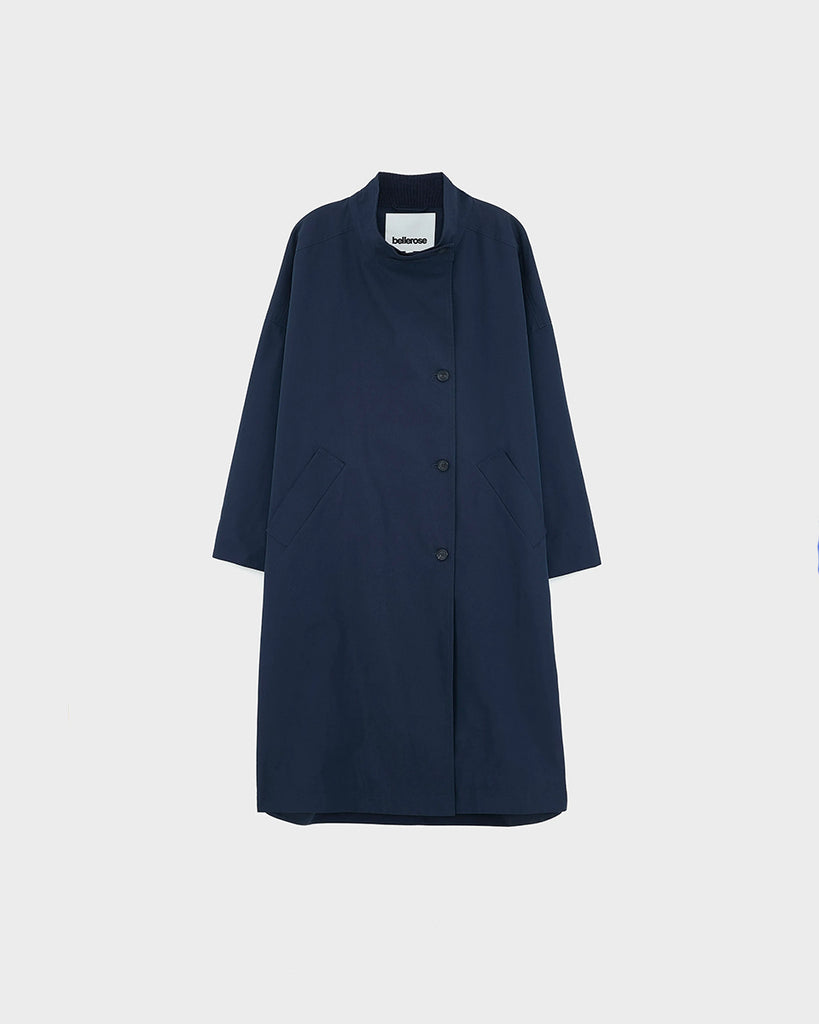 Długi, oversizowy, przejściowy trencz Juttac Bellerose z wysokim kołnierzem, opadającymi ramionami i luźnymi rękawami. Zapinany na jeden, boczny rząd guzików. Płaszcz ma prosty krój i głębokie, boczne rozcięcia zapinane na guziki. Posiada czerwoną podszewkę w kratę. 