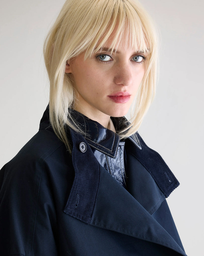 Długi, oversizowy, przejściowy trencz Juttac Bellerose z wysokim kołnierzem, opadającymi ramionami i luźnymi rękawami. Zapinany na jeden, boczny rząd guzików. Płaszcz ma prosty krój i głębokie, boczne rozcięcia zapinane na guziki. Posiada czerwoną podszewkę w kratę. 