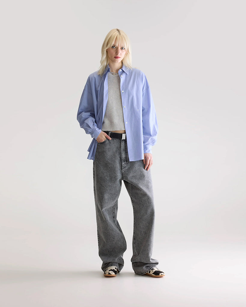 Niebieska, oversizowa koszula w cienkie prążki Gillian Bellerose z opadającymi ramionami i szerokimi rękawami zakończonymi wąskimi mankietami. Zapinana na guziki. Posiada bardzo ciekawą opcję asymetrycznego zapięcia i zwężenia w talii.