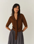 Cienki, brązowy sweter Bergen Scarf Cinnamon o dopasowanym kroju, z elastycznym ściagaczem w pasie i przy zakończeniach rękawów. Rękawy są długości do łokcia. Dekolt jest w nieco głębszy i okrągły z doszytym długim szalem, który można puścić luźno lub dowolnie związać. Wykonany w 100% z wełny merino.