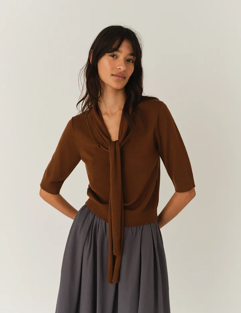 Cienki, brązowy sweter Bergen Scarf Cinnamon o dopasowanym kroju, z elastycznym ściagaczem w pasie i przy zakończeniach rękawów. Rękawy są długości do łokcia. Dekolt jest w nieco głębszy i okrągły z doszytym długim szalem, który można puścić luźno lub dowolnie związać. Wykonany w 100% z wełny merino.