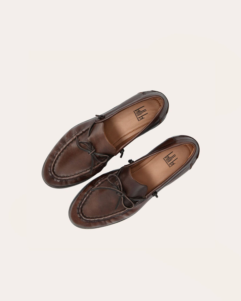 Ręcznie wykonane mokasyny marki Billi Bi Copenhagen z kasztanowej, gładkiej skóry, z okrągłym noskiem i skórzaną, sznurowaną kokardą. Przednia część buta ozdobiona jest wyrazistym ściegiem, który tworzy delikatne marszczenie na skórze, podkreślając ręczne wykończenie. Posiada 2,5 centymetrowy obcas.&nbsp;
