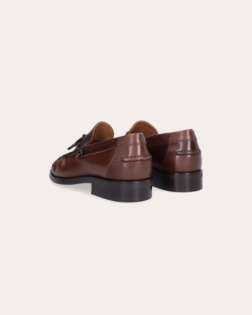 Ręcznie wykonane mokasyny marki Billi Bi Copenhagen z kasztanowej, gładkiej skóry, z okrągłym noskiem i skórzaną, sznurowaną kokardą. Przednia część buta ozdobiona jest wyrazistym ściegiem, który tworzy delikatne marszczenie na skórze, podkreślając ręczne wykończenie. Posiada 2,5 centymetrowy obcas.&nbsp;
