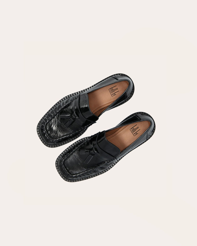 Ręcznie wykonane mokasyny marki Billi Bi Copenhagen z czarnej, lakierowanej skóry z kwadratowym noskiem. Mokasyny zdobi prosty pasek z przodu, a pod spodem dwa frędzle. W przedniej części buta znajduje się wyraźny szew, który tworzy delikatne marszczenie w skórze, podkreślając ręczne wykończenie. Buty mają 3 centymetrowy obcas.