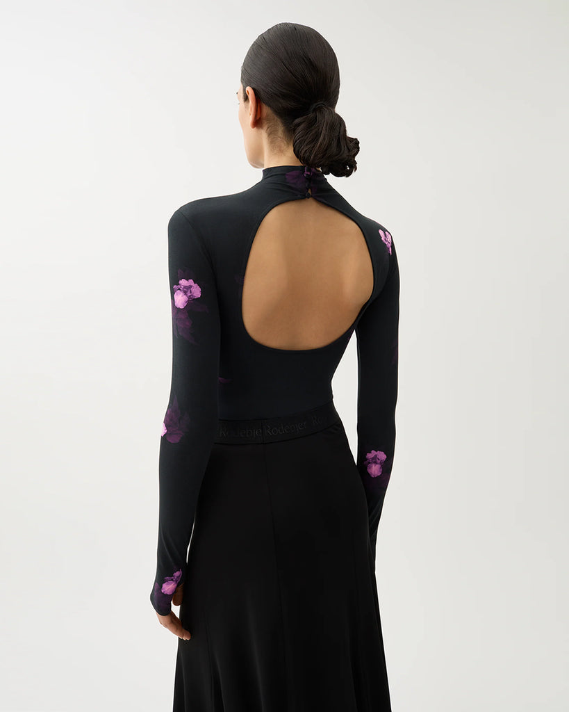 Czarne, przylegające Body Blake Bouquet Dark Purple w kwiatowy print z odkrytymi plecami i półgolfem zapinanym na guziki. Ma długie rękawy z otworami na kciuki. Wykonane z elastycznej bawełny. Świetnie sprawdzi się do eleganckich, wieczorowych stylizacji.