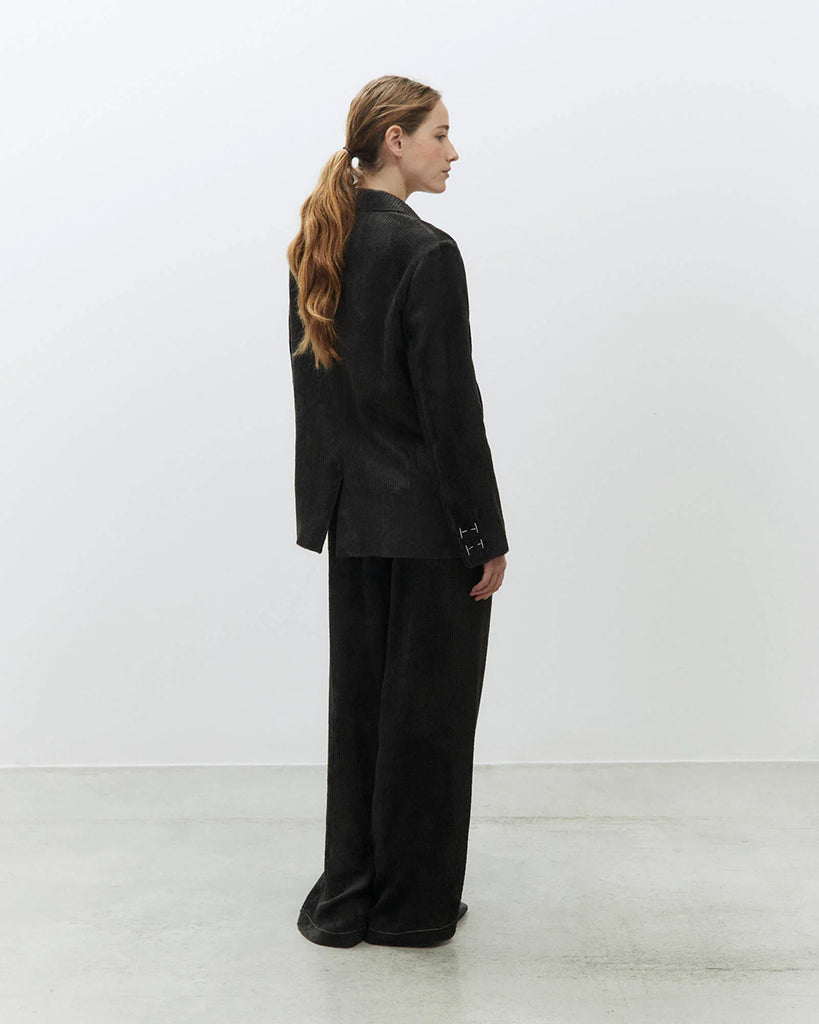 Jednorzędowa, sztruksowa marynarka Velvet Rib Carbone o klasycznym kroju z kontrastującymi kremowymi przeszyciami przy mankietach. Zapinana na guzik z przodu. Posiada kieszenie z wypustkami i rozcięcie z tyłu. Stwórz idealny look ze spodniami Velvet Rib Carbone.