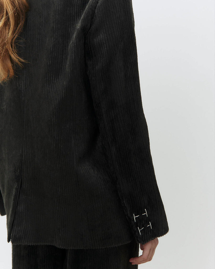 Jednorzędowa, sztruksowa marynarka Velvet Rib Carbone o klasycznym kroju z kontrastującymi kremowymi przeszyciami przy mankietach. Zapinana na guzik z przodu. Posiada kieszenie z wypustkami i rozcięcie z tyłu. Stwórz idealny look ze spodniami Velvet Rib Carbone.