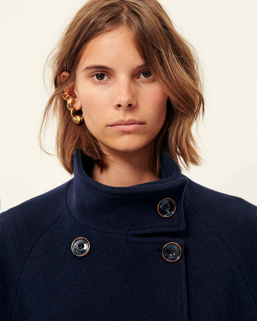 Klasyczny, oversizowy, granatowy płaszcz Bleeckett Indigo o prostym i eleganckim kroju. Ma dwurzędowe zapięcie, z dwoma symetrycznymi rzędami dużych, ciemnych guzików oraz kołnierz typu stójka. Kieszenie wpuszczane po bokach, na wysokości bioder. Sięga mniej więcej do połowy łydki, co nadaje mu klasyczny, zimowy charakter.&nbsp;
