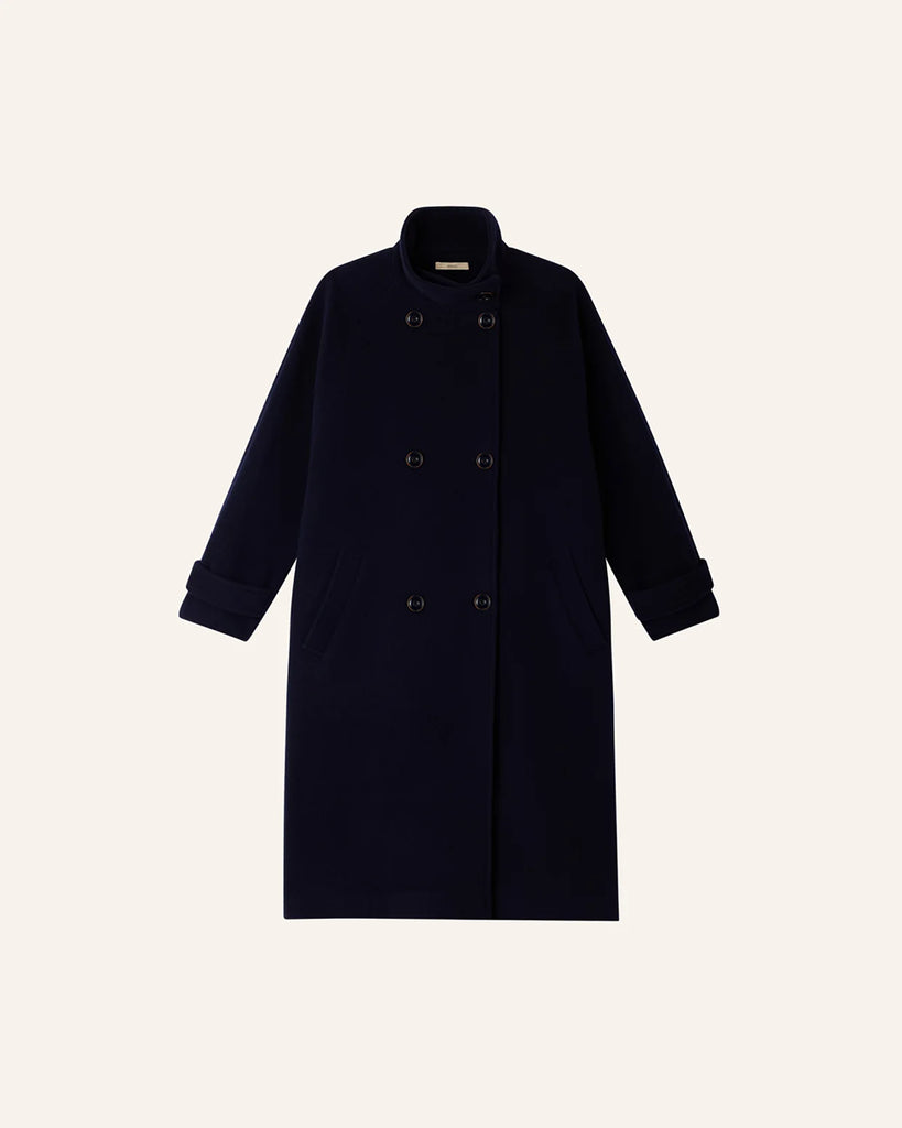 Klasyczny, oversizowy, granatowy płaszcz Bleeckett Indigo o prostym i eleganckim kroju. Ma dwurzędowe zapięcie, z dwoma symetrycznymi rzędami dużych, ciemnych guzików oraz kołnierz typu stójka. Kieszenie wpuszczane po bokach, na wysokości bioder. Sięga mniej więcej do połowy łydki, co nadaje mu klasyczny, zimowy charakter.&nbsp;
