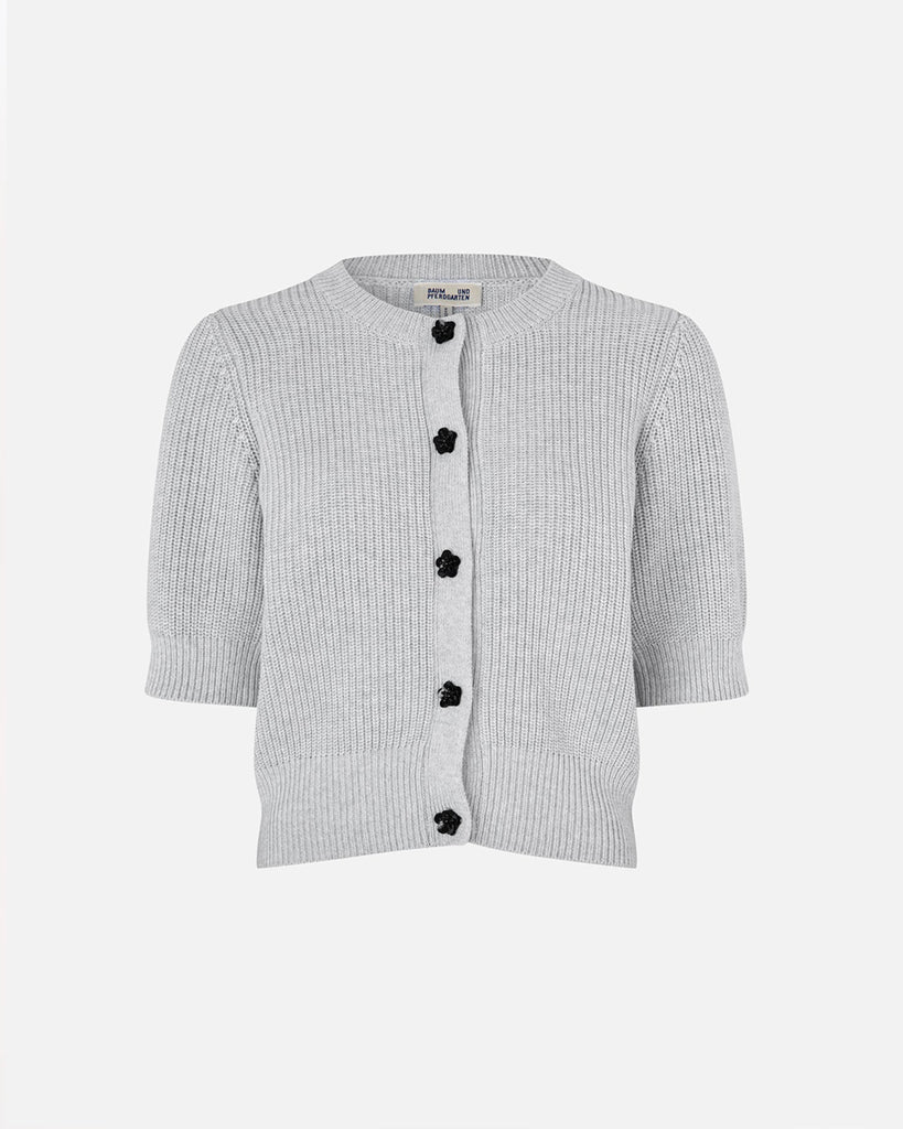 Dzianinowy, krótki kardigan Cathia Grey Melange z krótkim rękawem, o lekko dopasowanym kroju. Zapinany na zatrzaski zdobione błyszczącymi kwiatami. Wykonany z bawełny organicznej. Sweterek zestaw ze swoimi ulubionymi jeansami lub spódnicą.