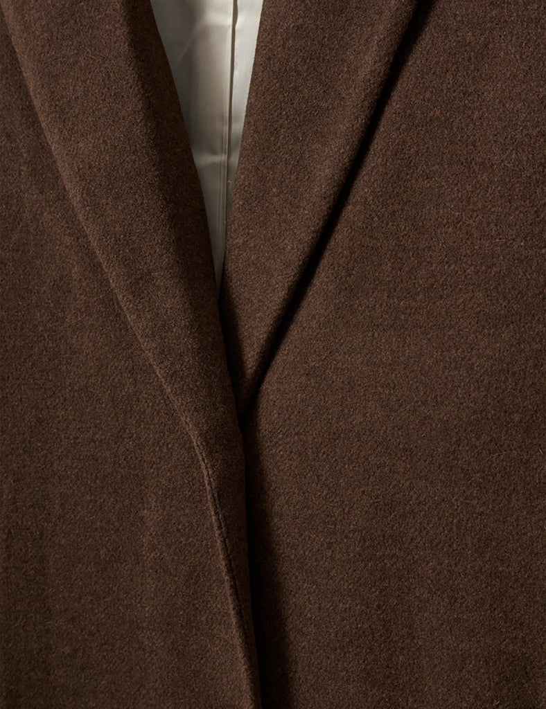 Elegancki, prosty płaszcz Clooney Man Brown w pięknym, czekoladowym kolorze z klasycznym kołnierzem i bocznymi kieszeniami. Płaszcz ma prosty krój i długość przed kostki. Zapinany z przodu na guziki. Posiada podszewkę. To ponadczasowy, klasyczny fason idealny na chłodniejsze jesienne i zimowe dni. Wykonany z mieszanki wełny z recyklingu.&nbsp;