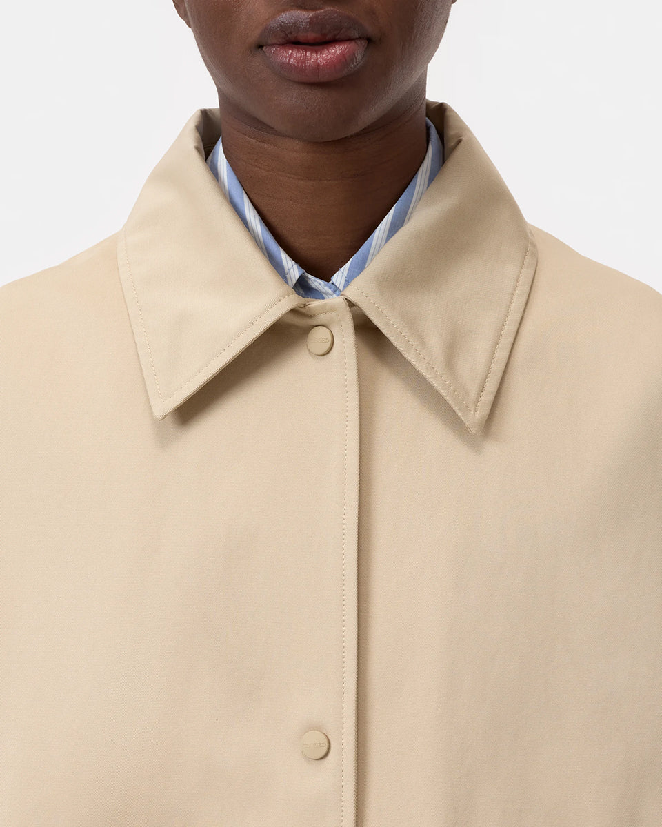 Cienki, krótki, beżowy płaszcz Short coat 97949 CLOSED o luźnym fasonie i prostym kroju. Posiada szerokie, długie rękawy, kołnierzyk i duże, przednie kieszenie z klapkami. Zapinany za pomocą zatrzaskowych guzików
