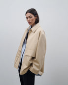 Cienki, krótki, beżowy płaszcz Short coat 97949 CLOSED o luźnym fasonie i prostym kroju. Posiada szerokie, długie rękawy, kołnierzyk i duże, przednie kieszenie z klapkami. Zapinany za pomocą zatrzaskowych guzików