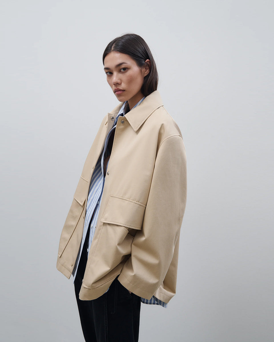 Cienki, krótki, beżowy płaszcz Short coat 97949 CLOSED o luźnym fasonie i prostym kroju. Posiada szerokie, długie rękawy, kołnierzyk i duże, przednie kieszenie z klapkami. Zapinany za pomocą zatrzaskowych guzików