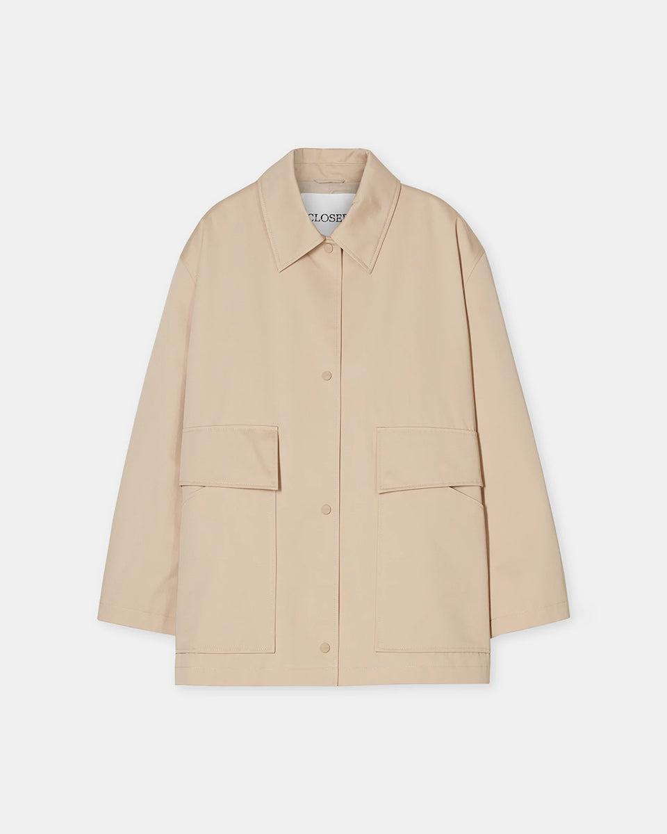 Cienki, krótki, beżowy płaszcz Short coat 97949 CLOSED o luźnym fasonie i prostym kroju. Posiada szerokie, długie rękawy, kołnierzyk i duże, przednie kieszenie z klapkami. Zapinany za pomocą zatrzaskowych guzików
