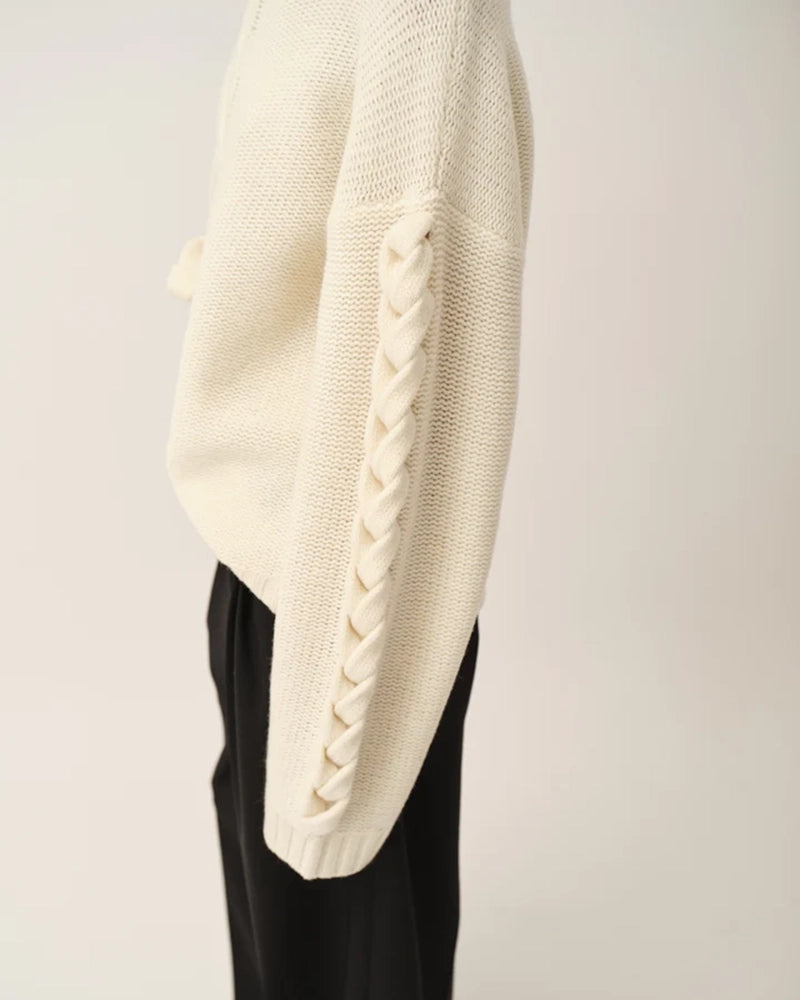 Luźny, gruby, kremowy golf Como Braid The Garment z pięknymi, warkoczowymi i wzorami. Posiada opadające ramiona i szeroki, zaokrąglone rękawy. Wykończony ściągaczami o prążkowanej fakturze. Sweter ma długość za biodra. Wykonany bardzo ciepłej i miękkiej, wełnianej dzianiny z kaszmirem. 