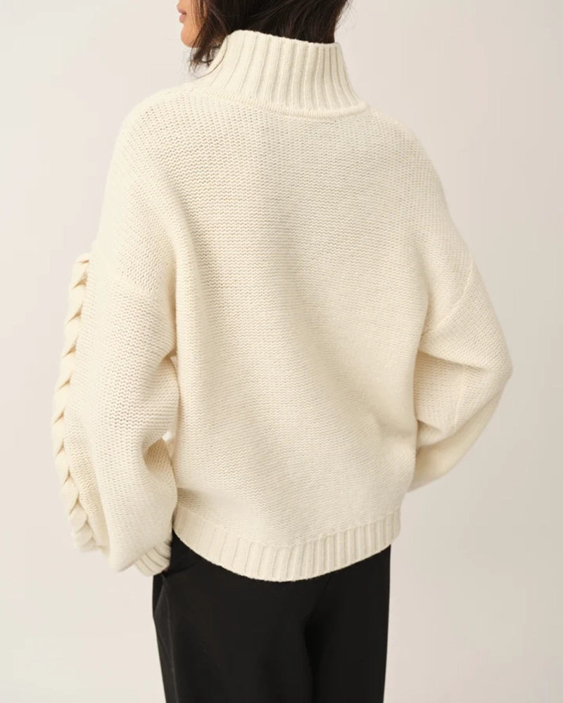 Luźny, gruby, kremowy golf Como Braid The Garment z pięknymi, warkoczowymi i wzorami. Posiada opadające ramiona i szeroki, zaokrąglone rękawy. Wykończony ściągaczami o prążkowanej fakturze. Sweter ma długość za biodra. Wykonany bardzo ciepłej i miękkiej, wełnianej dzianiny z kaszmirem. 