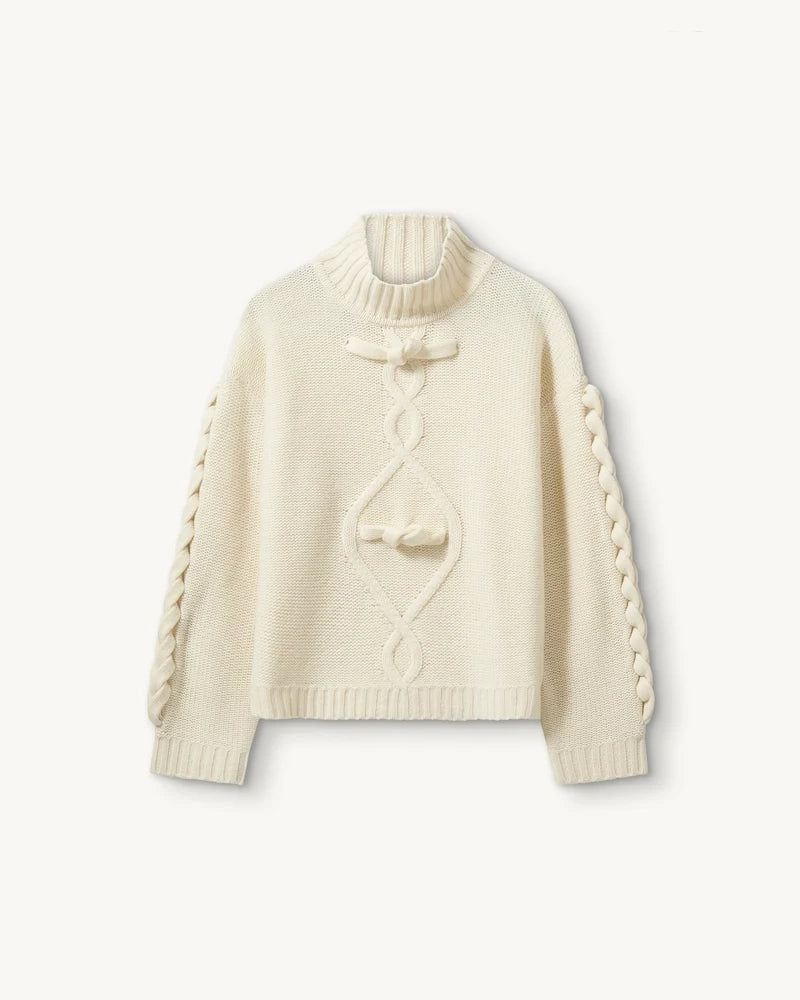 Luźny, gruby, kremowy golf Como Braid The Garment z pięknymi, warkoczowymi i wzorami. Posiada opadające ramiona i szeroki, zaokrąglone rękawy. Wykończony ściągaczami o prążkowanej fakturze. Sweter ma długość za biodra. Wykonany bardzo ciepłej i miękkiej, wełnianej dzianiny z kaszmirem. 