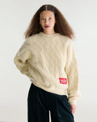 Sweter o luźnym kroju i okrągłym dekolcie Dole Ivory marki Bellerose wykonany z dzianiny w kolorze ecru o splocie ściągaczowym z motywem warkoczowym. Wyróżnia się obszerną górną częścią, zwężanym dołem, krótszym, dwuwarstwowym wykończeniem dekoltu oraz zewnętrzną naszywką.&nbsp;

-Luźny krój: zapewnia więcej swobody i komfortu w obrębie klatki piersiowej oraz ramion

-Splot ściągaczowy 1x1 z motywem warkoczowym

-Zwężany dół
